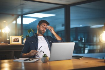 Man sitting at desk in office rubbing head, stressed
