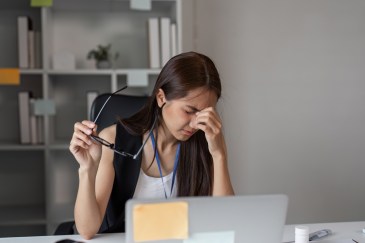 A young woman pinches her nose in frustration while at her desk.