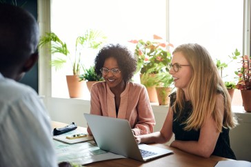 Women sitting next to each other in office with laptop