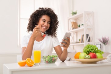 Woman looking at her phone, smiling, eating salad, healthy