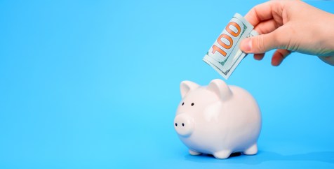 Hand putting $100 bill in piggybank