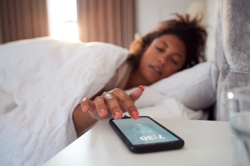 A woman reaches her arm out of bed to turn off the alarm on her phone.