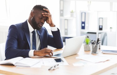Man sitting at desk looking at laptop, frustrated