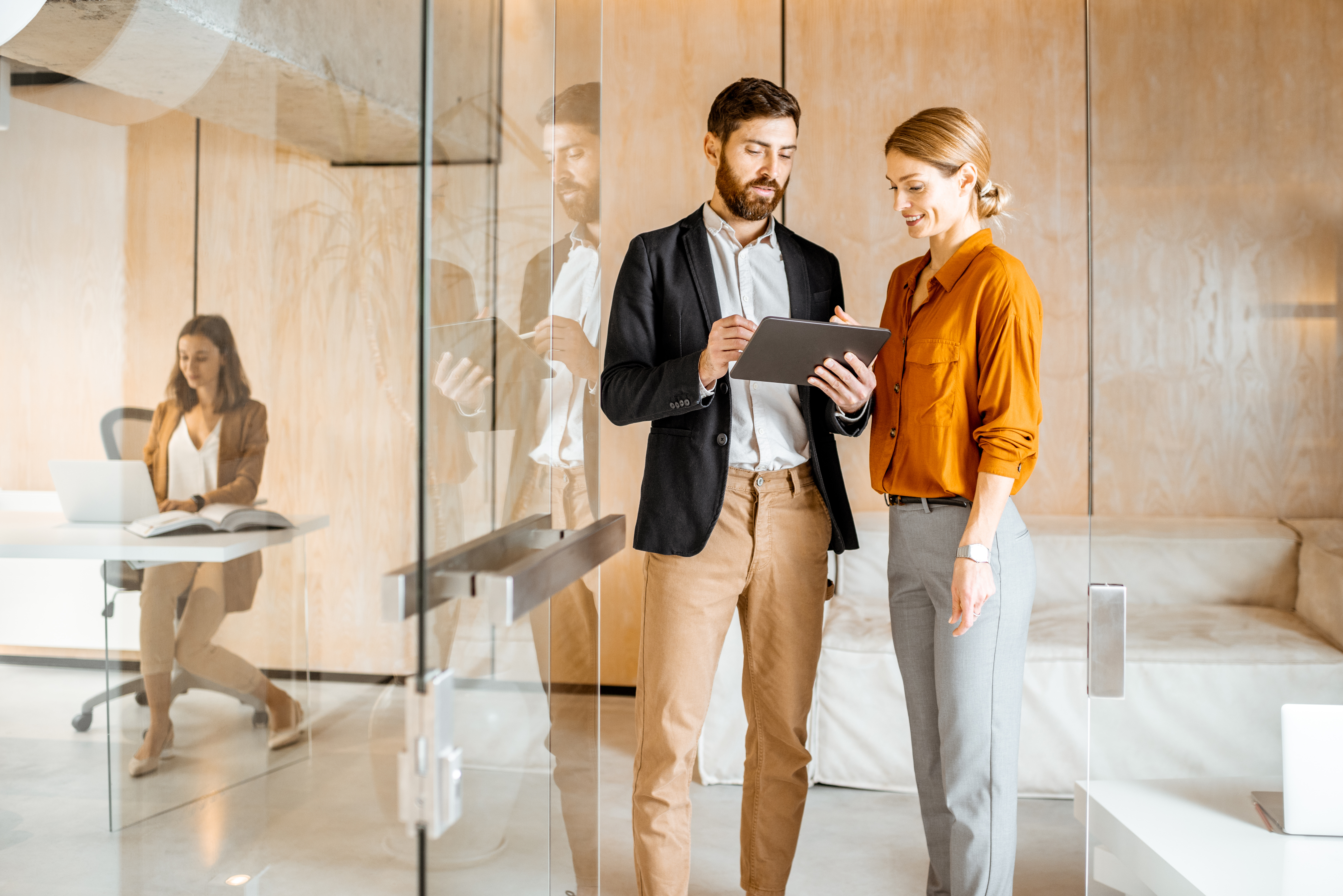 Man and woman standing in hall of office looking at tablet.