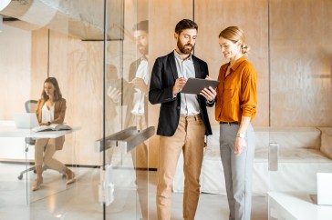 Man and woman standing in hall of office looking at tablet.