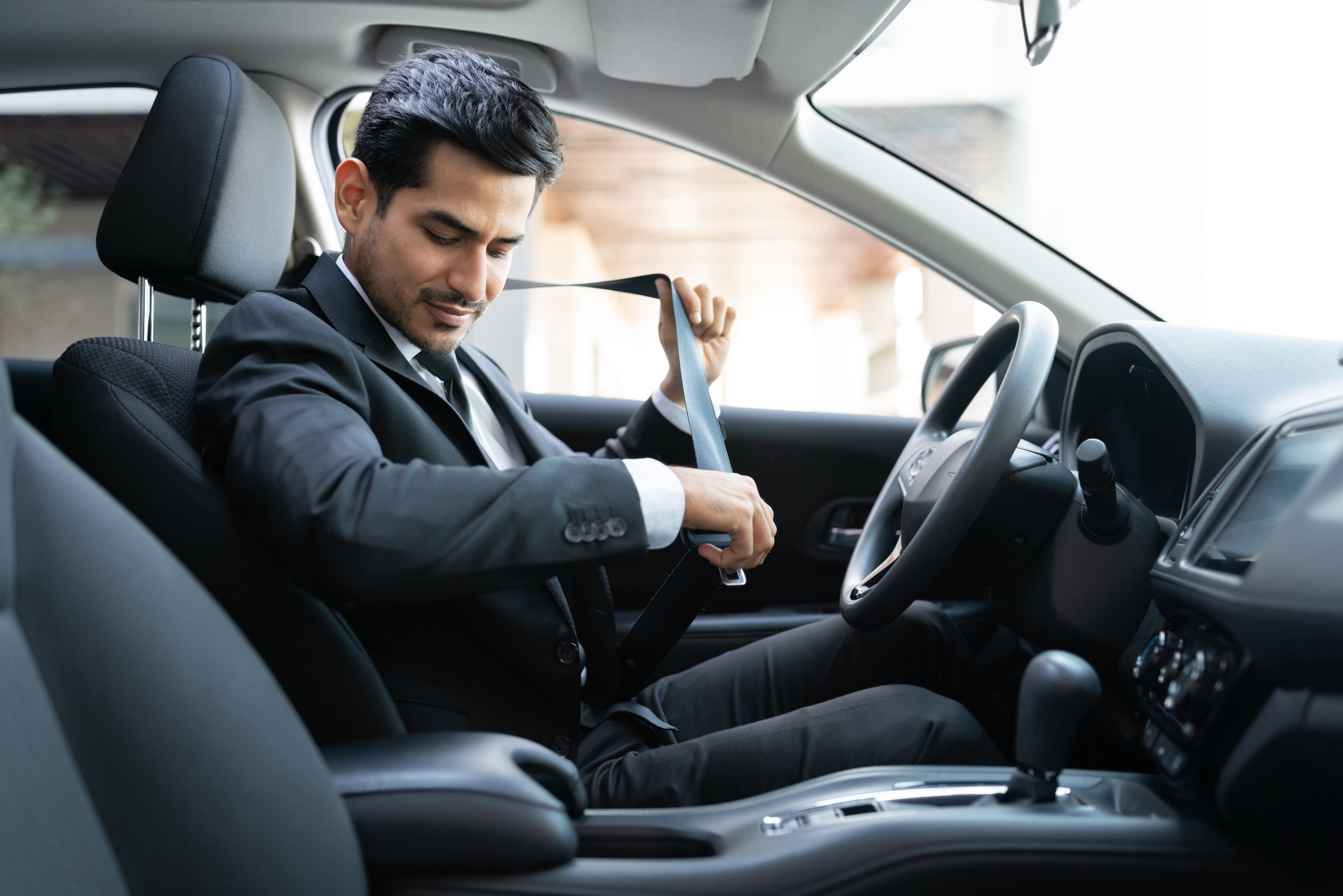 Man in suit sitting in car buckling seatbelt