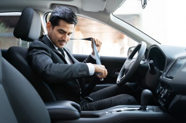 Man in suit sitting in car buckling seatbelt