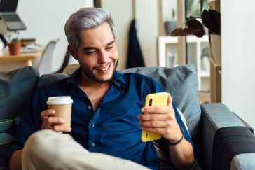 Man holding coffee and looking at phone, smiling