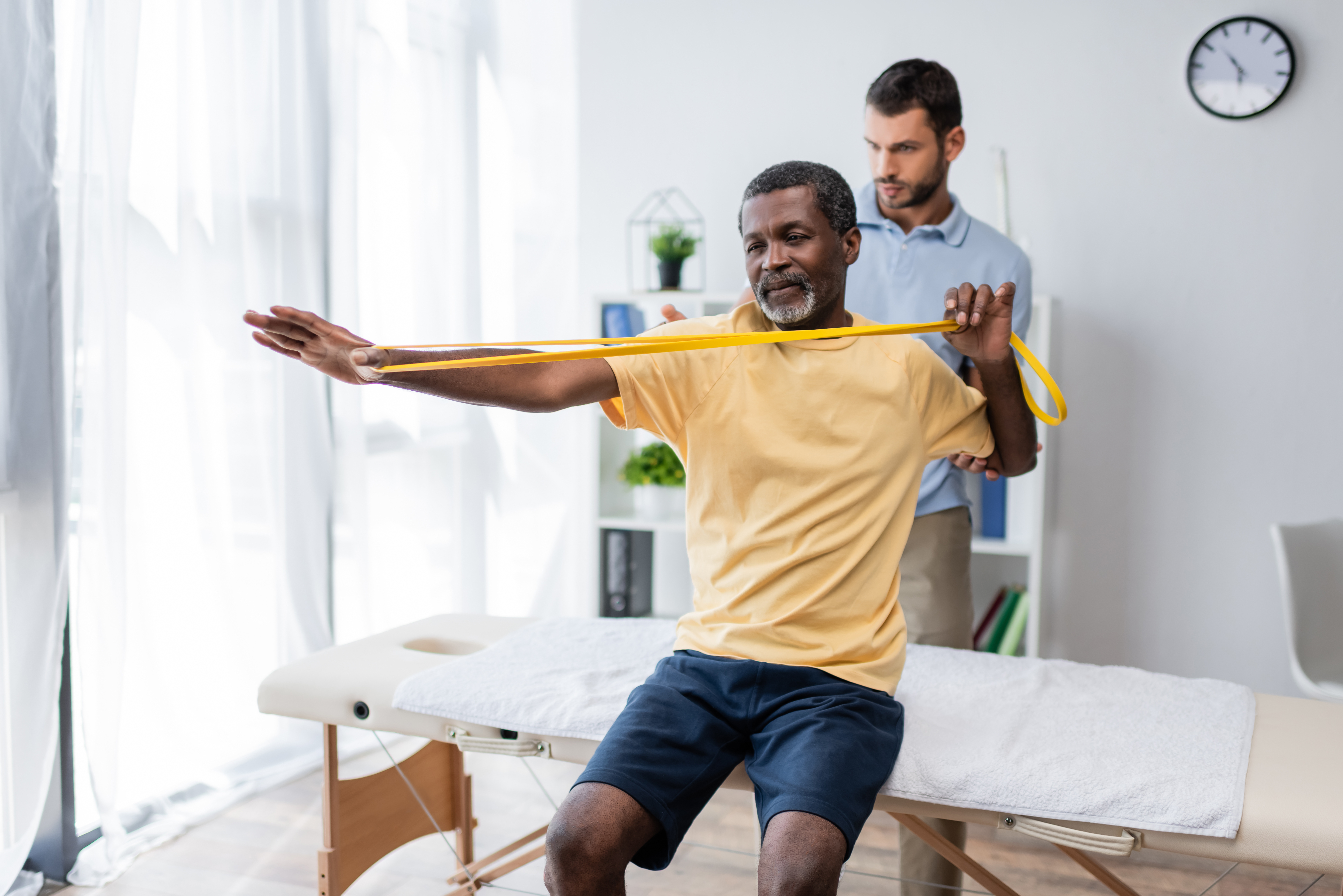 Physical therapist helping man do exercises with resistance band