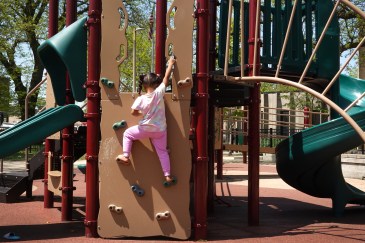 A little kid is climbing up a jungle gym.