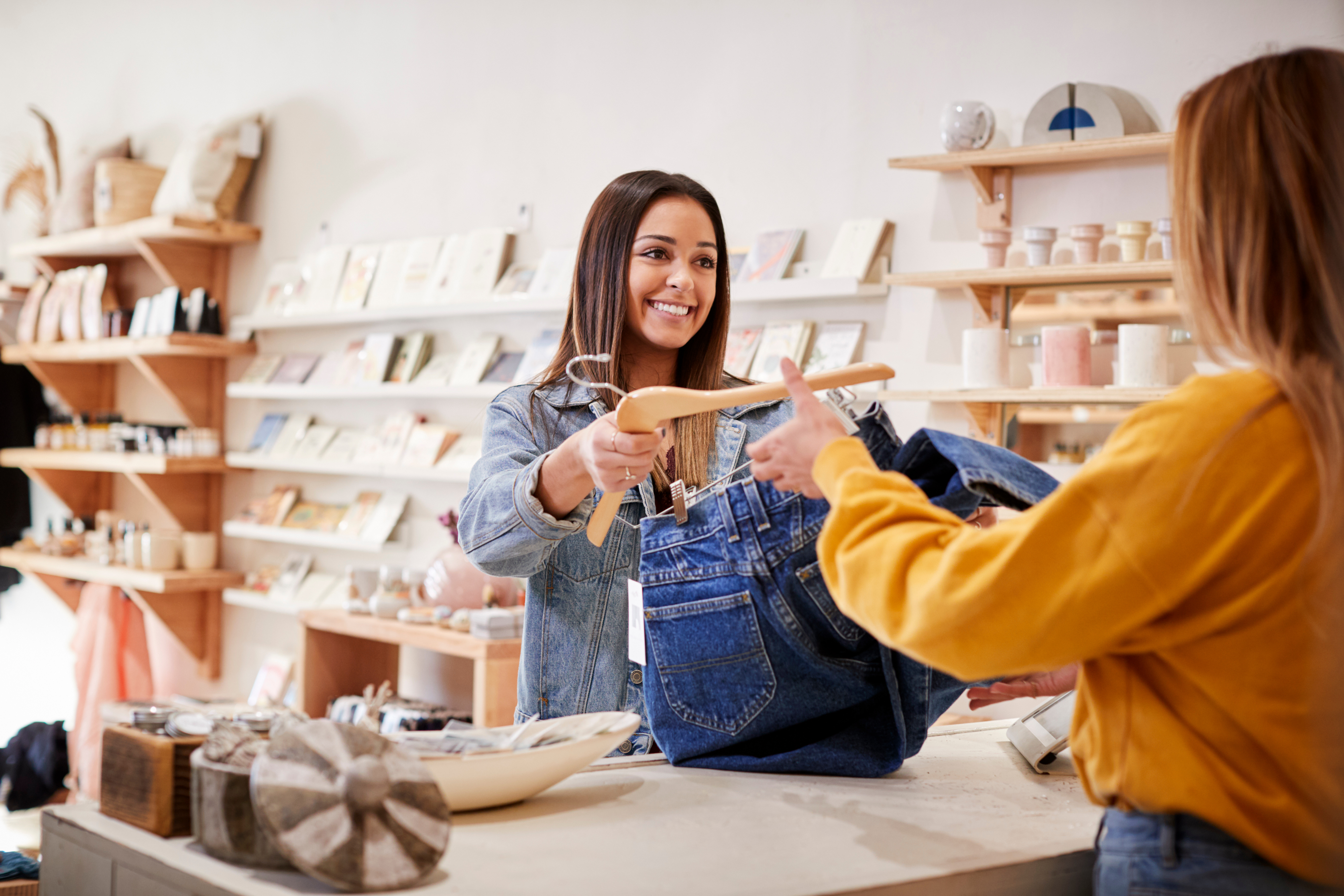 Woman in retail shop handing jeans to cashier