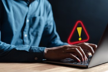 Man typing on the computer with a red warning sign