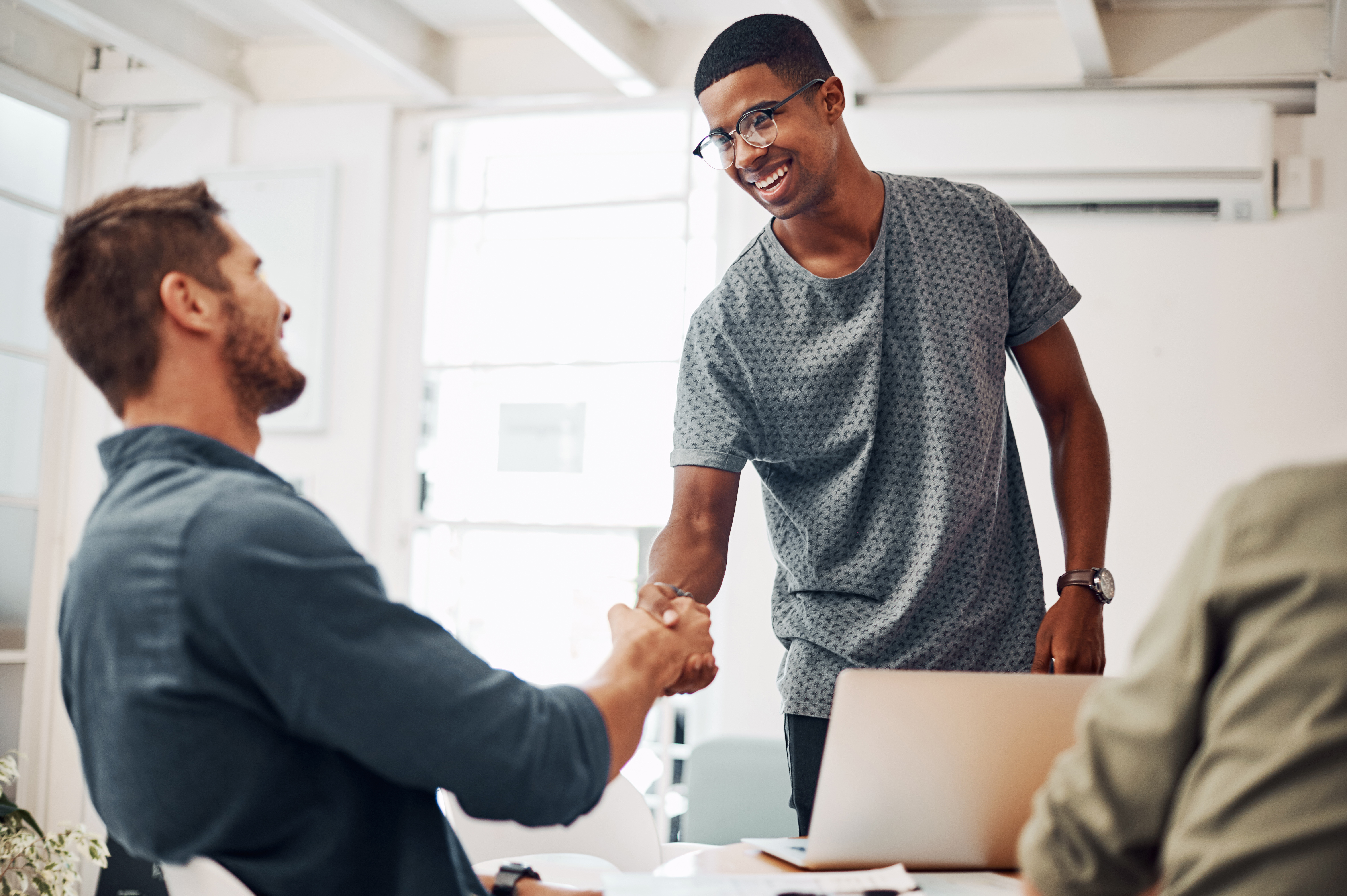 Young male standing up shaking hands with man sitting