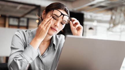 A woman rubs her eyes in irritation while holding her glasses off her face.
