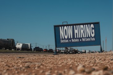 A billboard that says "Now Hiring" alongside a freeway.