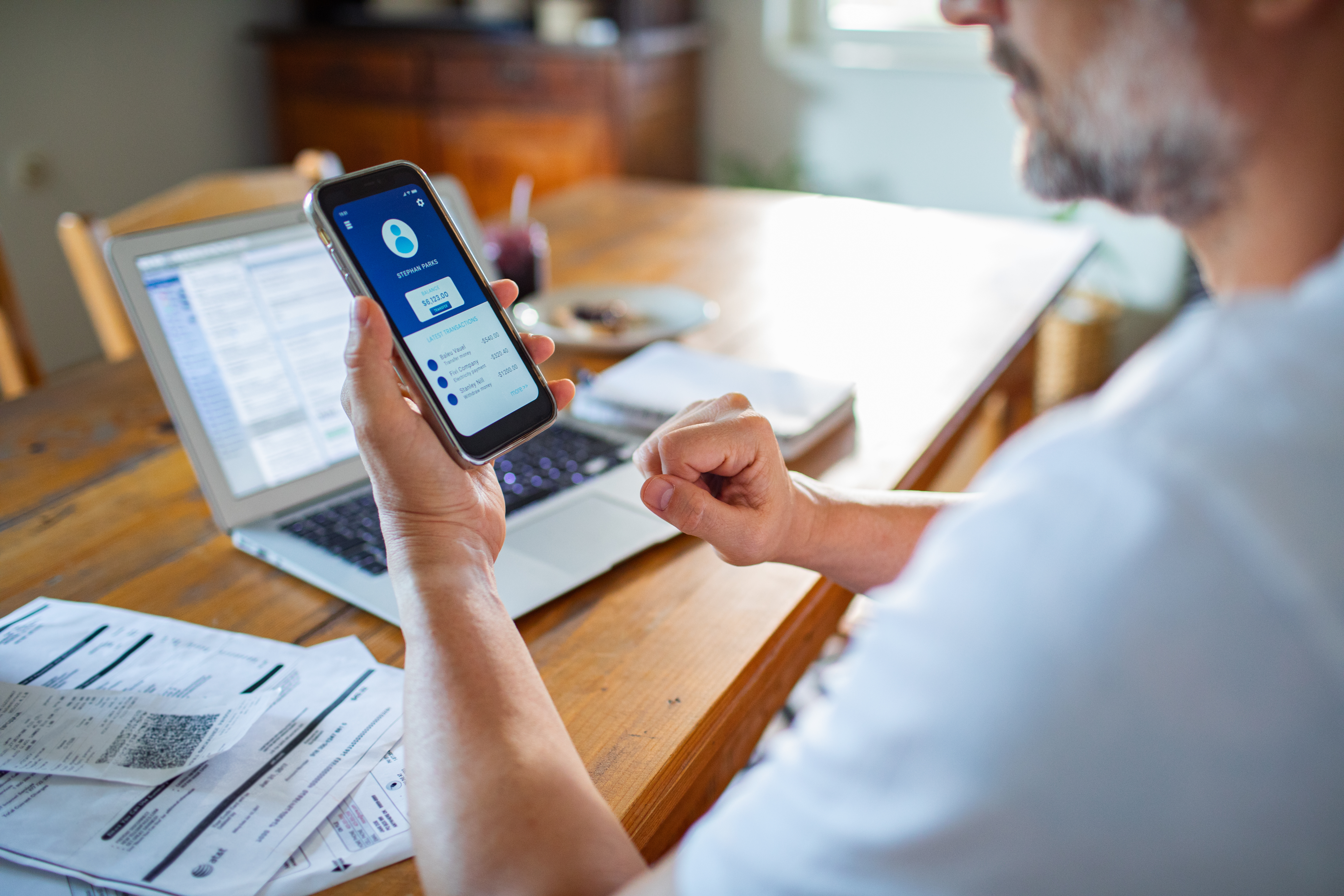Man looking at cell phone, personal account, laptop on table