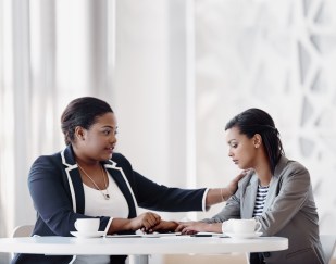 Two female employees, one holding other's hand, showing care and compassion