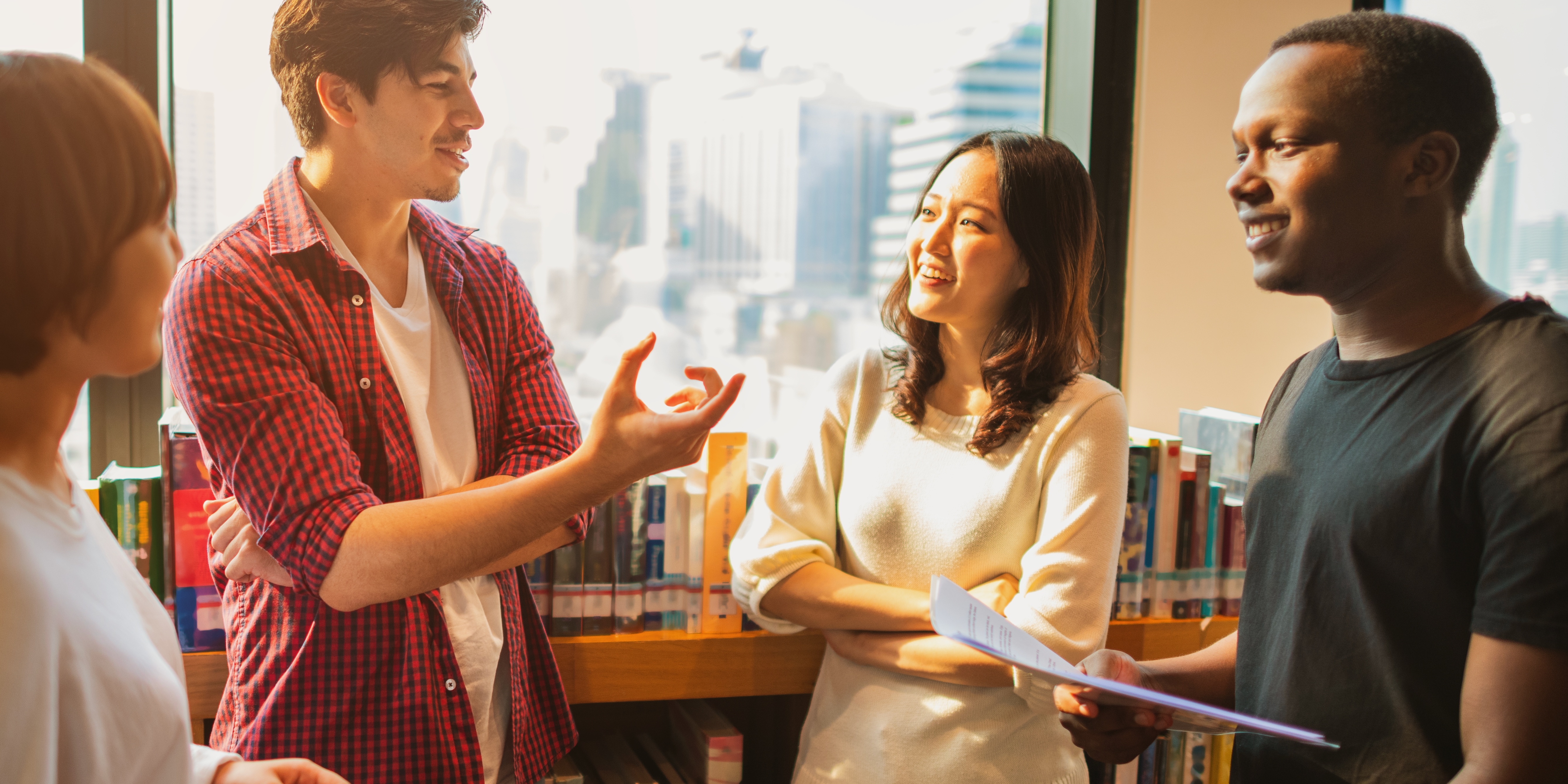 Group of young people standing near shelf of books talking