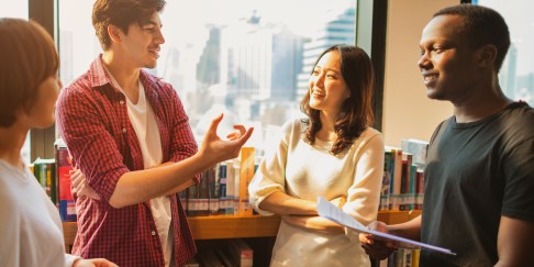 Group of young people standing near shelf of books talking