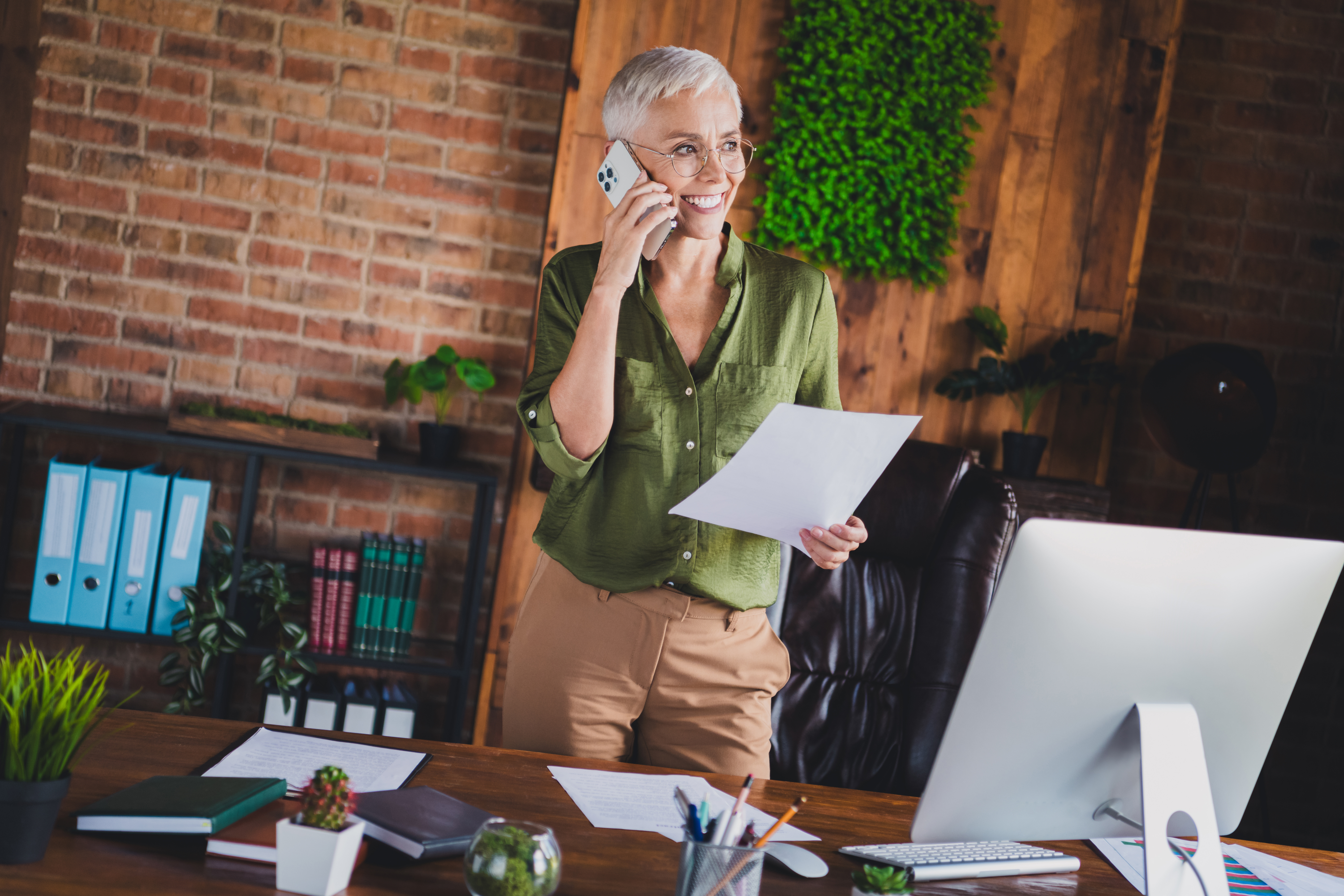 Woman with short gray hair in office talking on phone, holding paper