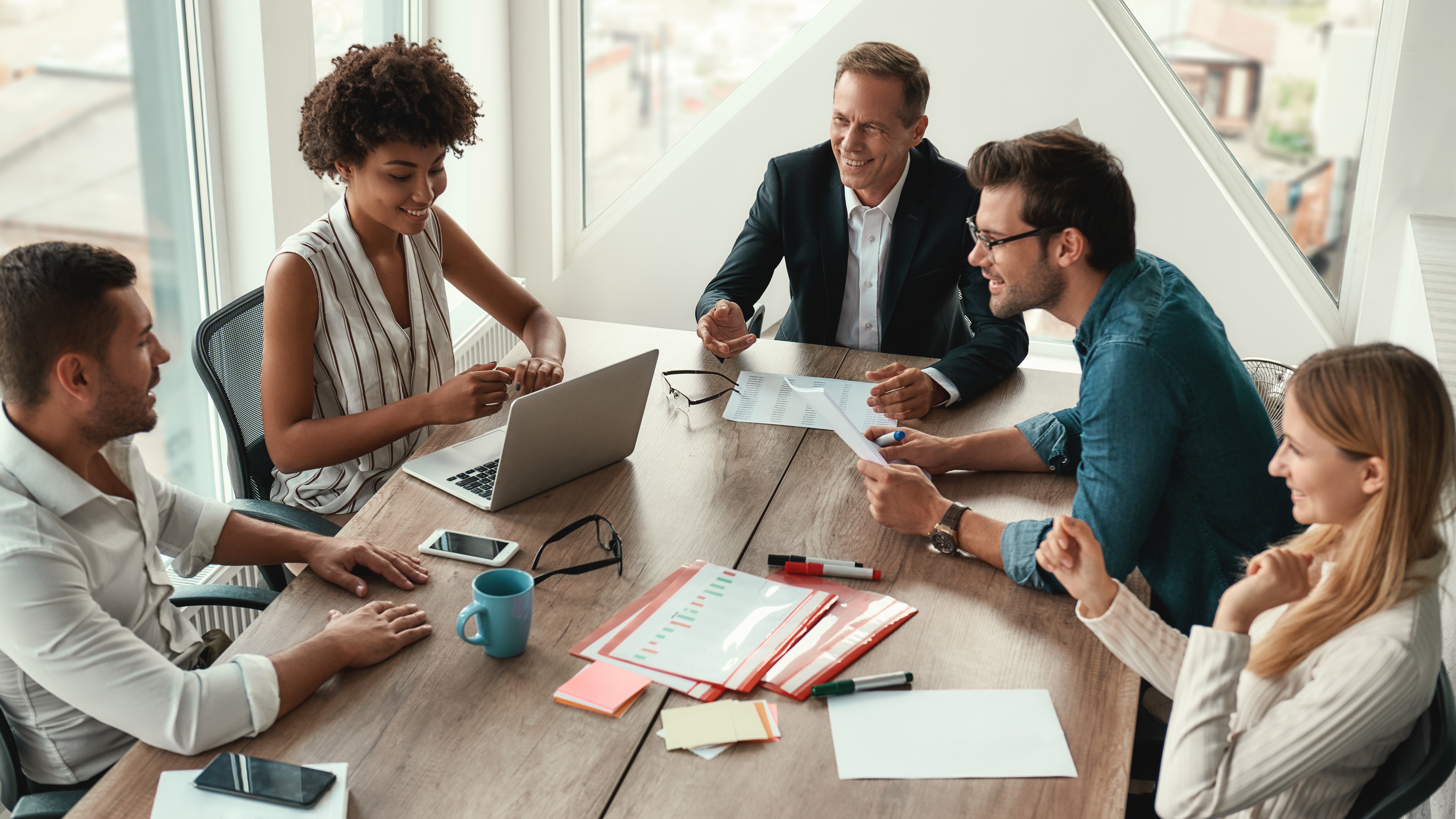 Employees sitting around table, working, smiling