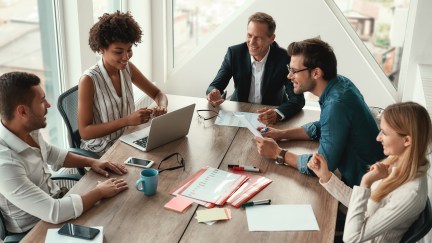 Employees sitting around table, working, smiling