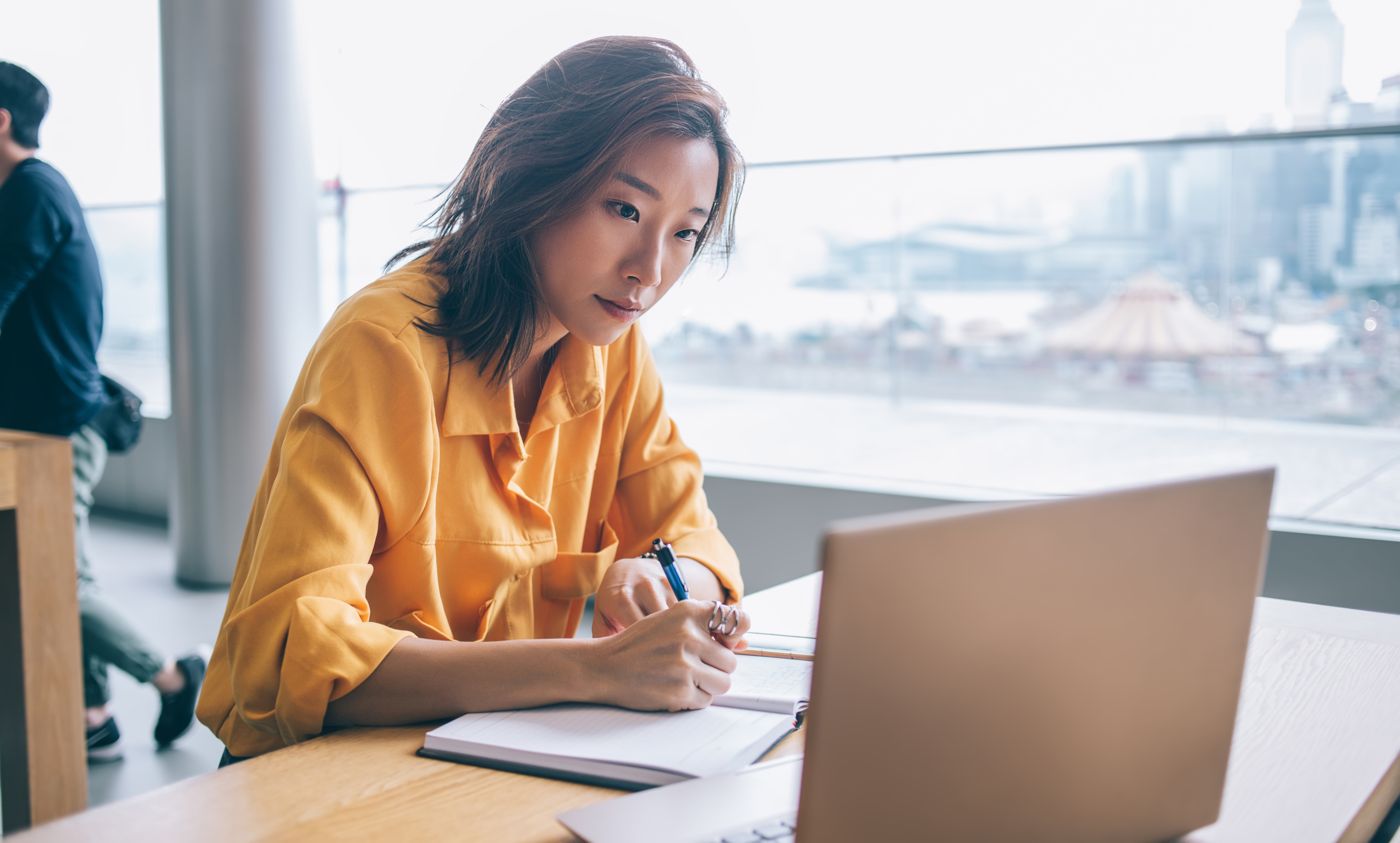 Woman writing on pad, and looking at laptop