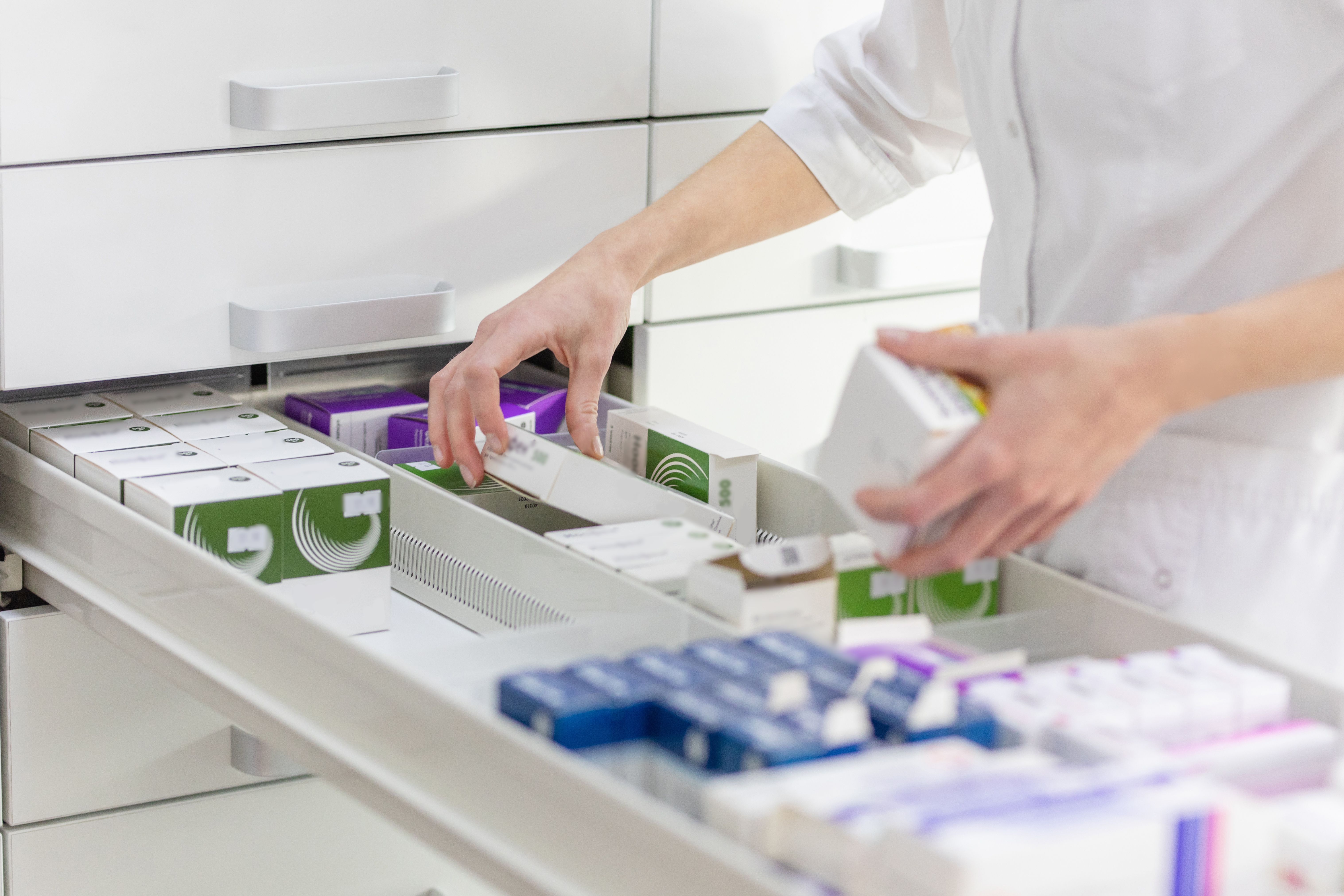 A pharmacist is organizing medication in a long drawer.