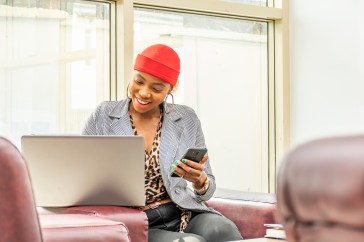 Younger woman looking at a computer while holding a cell phone