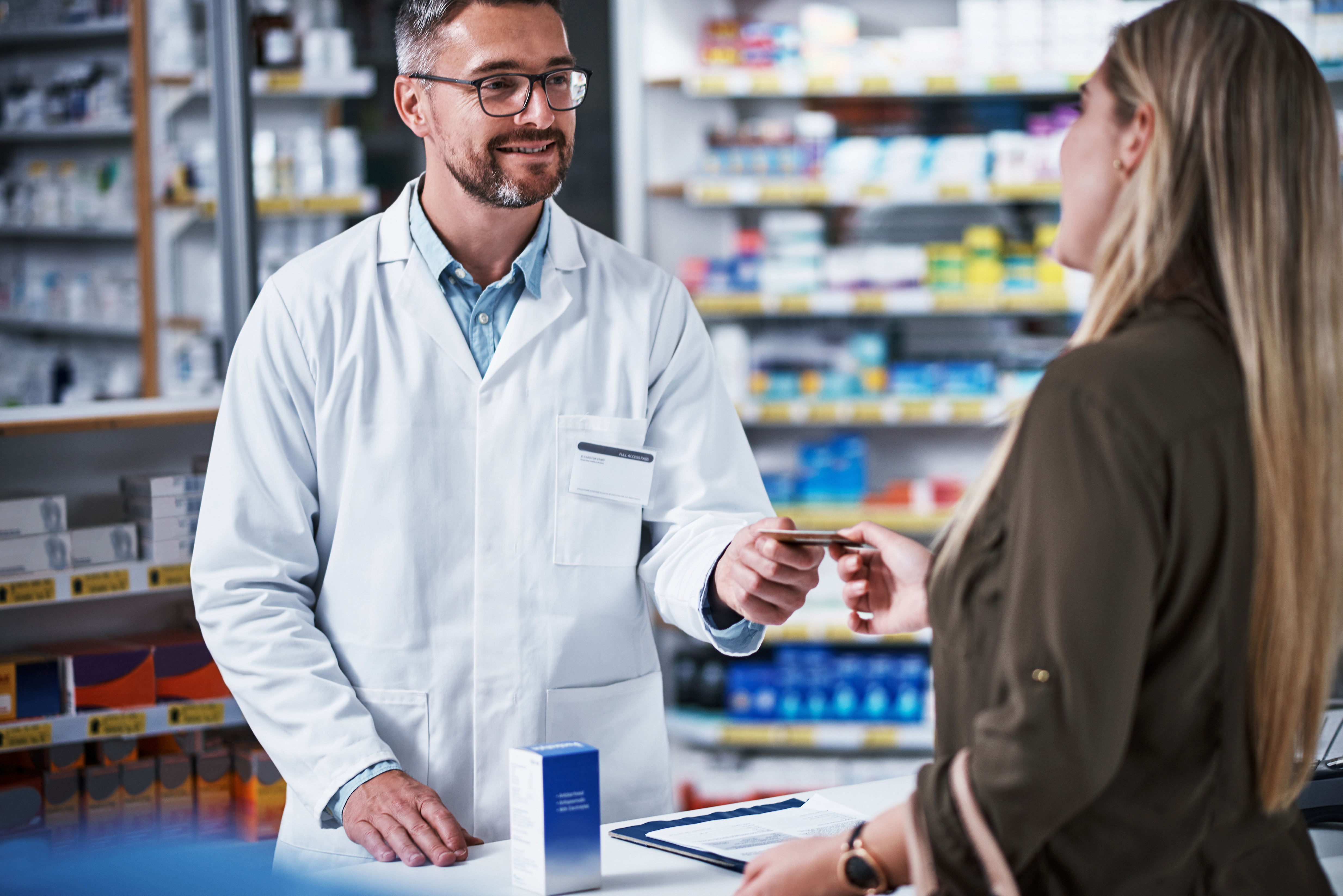 Woman handing pharmacist card, standing at pharmacy counter