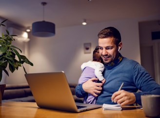 Dad holding baby while looking at laptop, taking notes