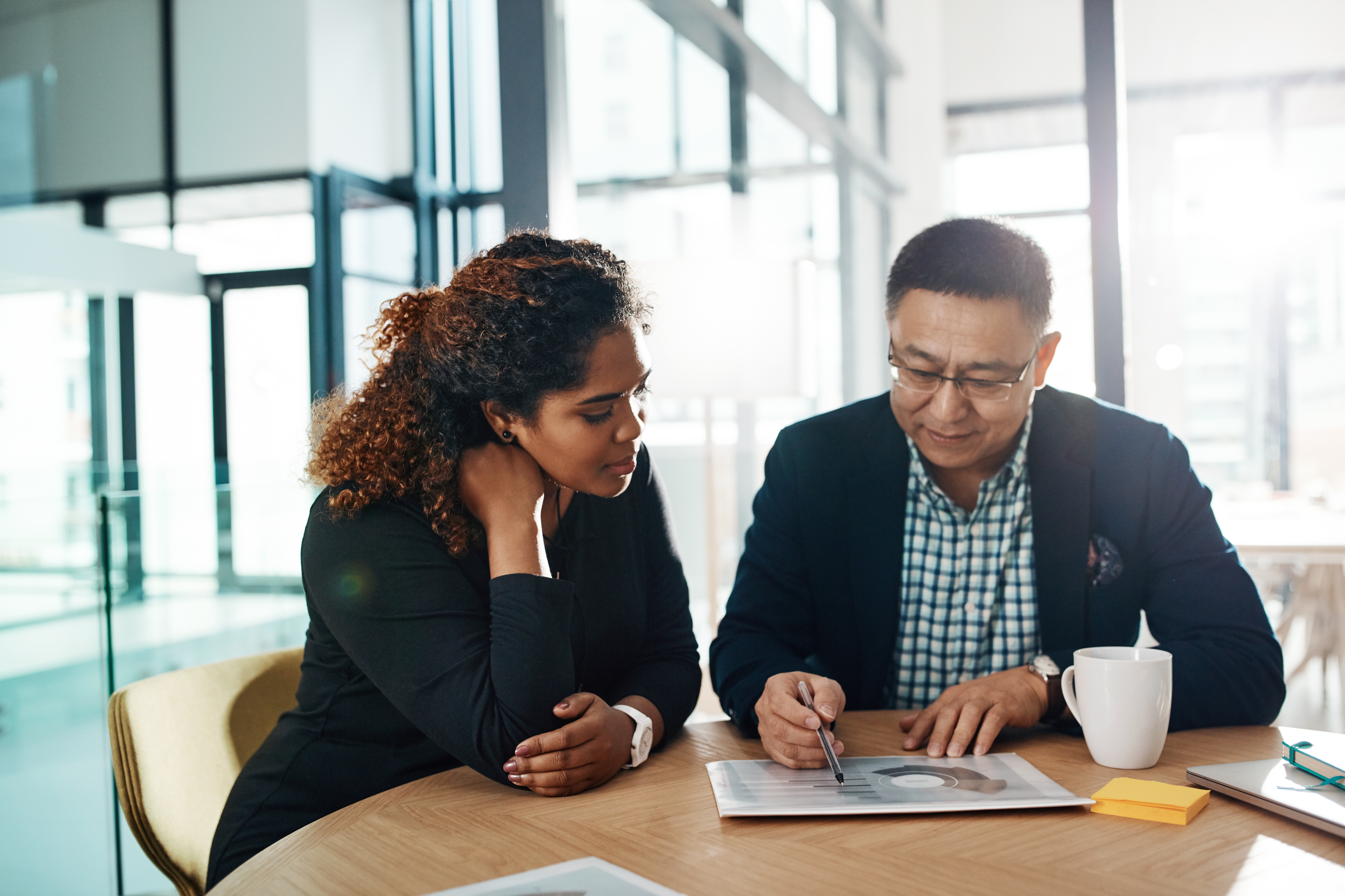 Employees working with each other, looking at paper, mug on table