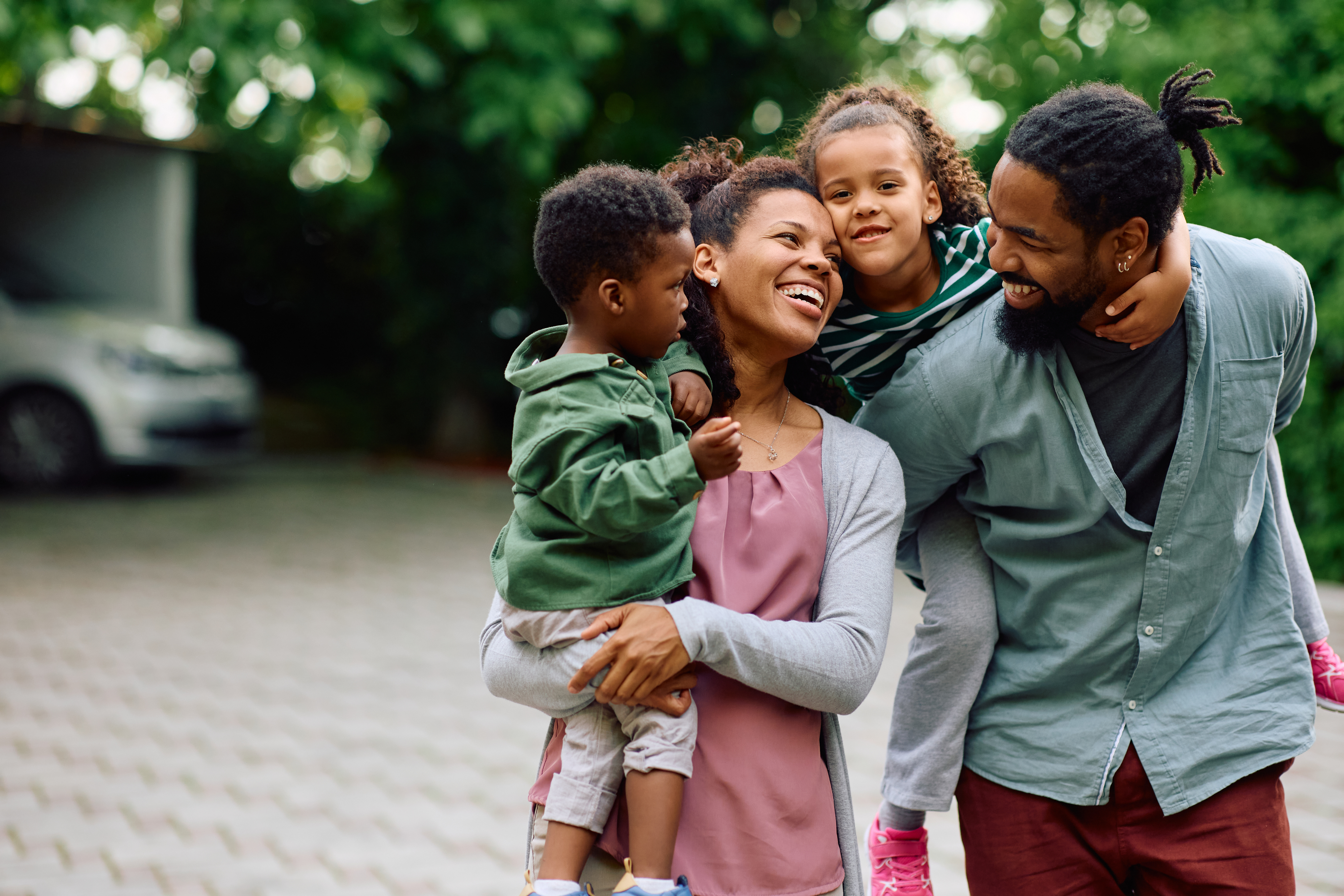 A Black family of four is walking down the driveway together, smiling at each other.