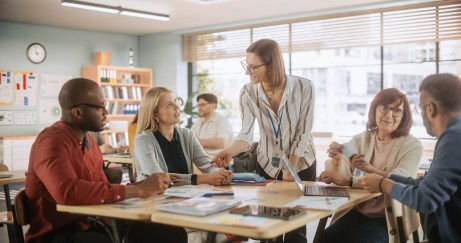 Woman wearing glasses, standing, working with group of employees sitting around table