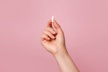Hand holding white pill, pink background