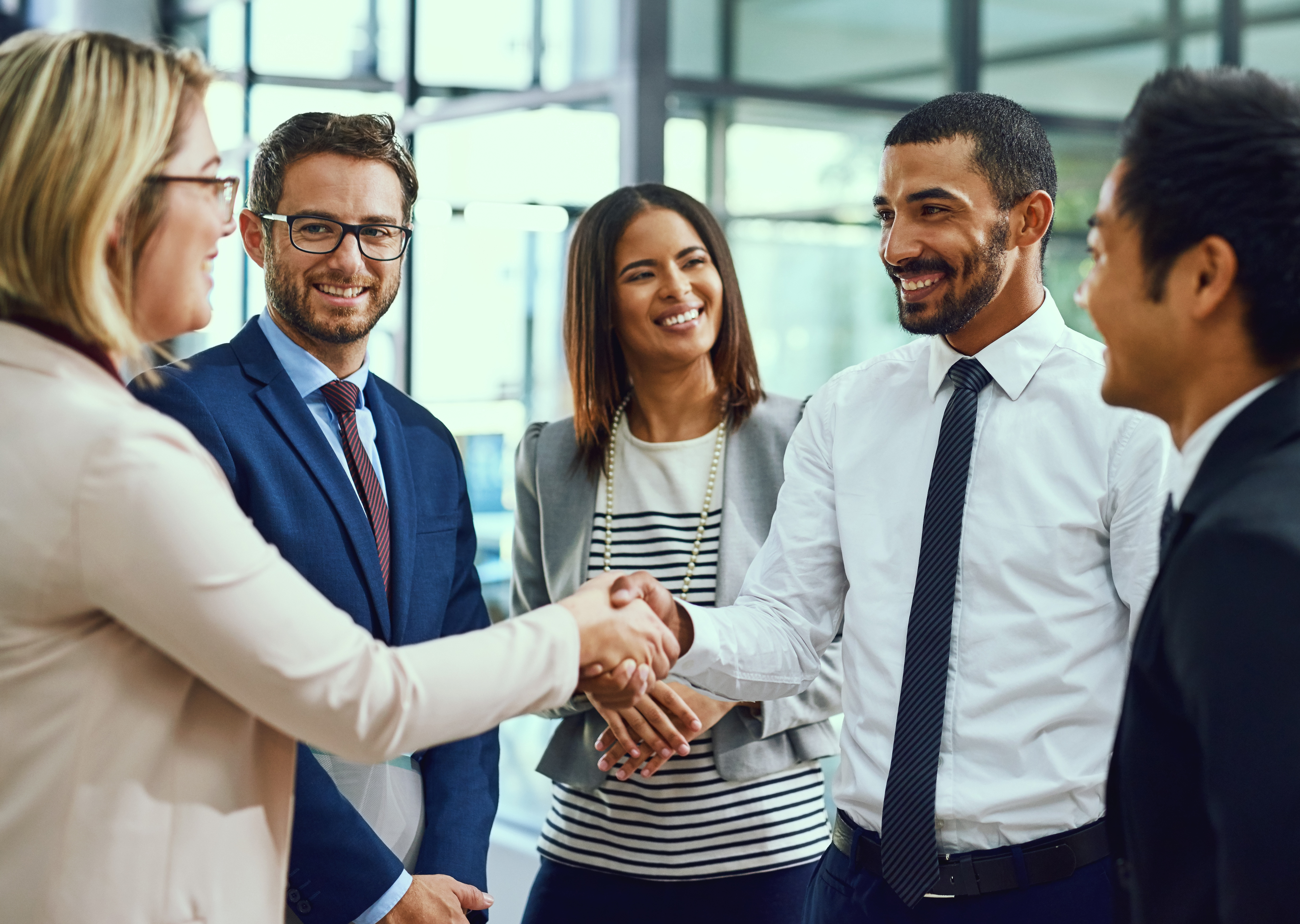 Male and female employees shaking hands, others standing, smiling