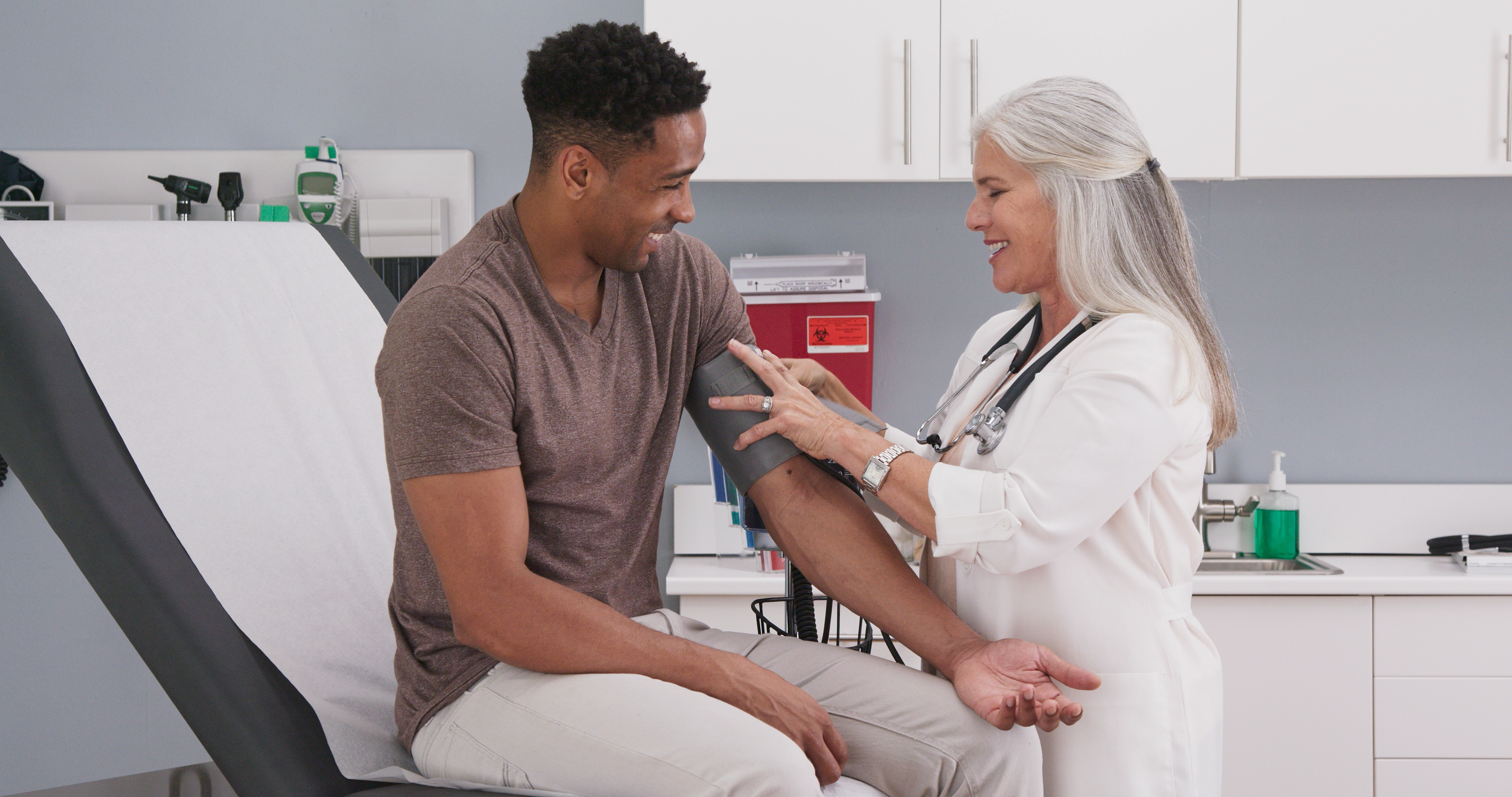 Female doctor taking blood pressure of young male patient, both smling