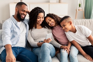 Family with two small children sitting on couch looking at smart phone
