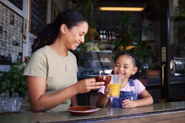 Mom and daughter, clinking drinks with coffee and orange juice, smiling