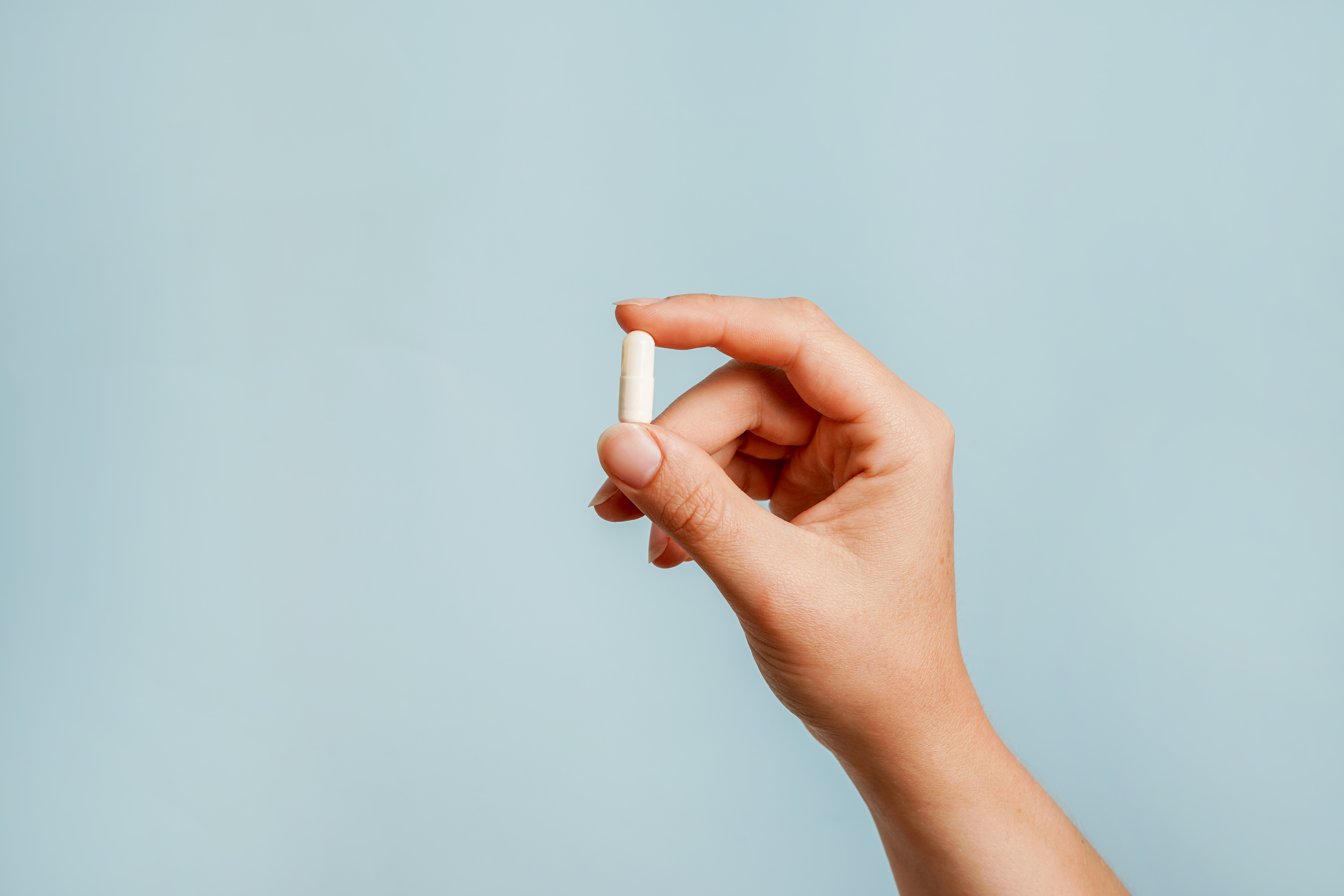 Hand holding pill between two fingers
