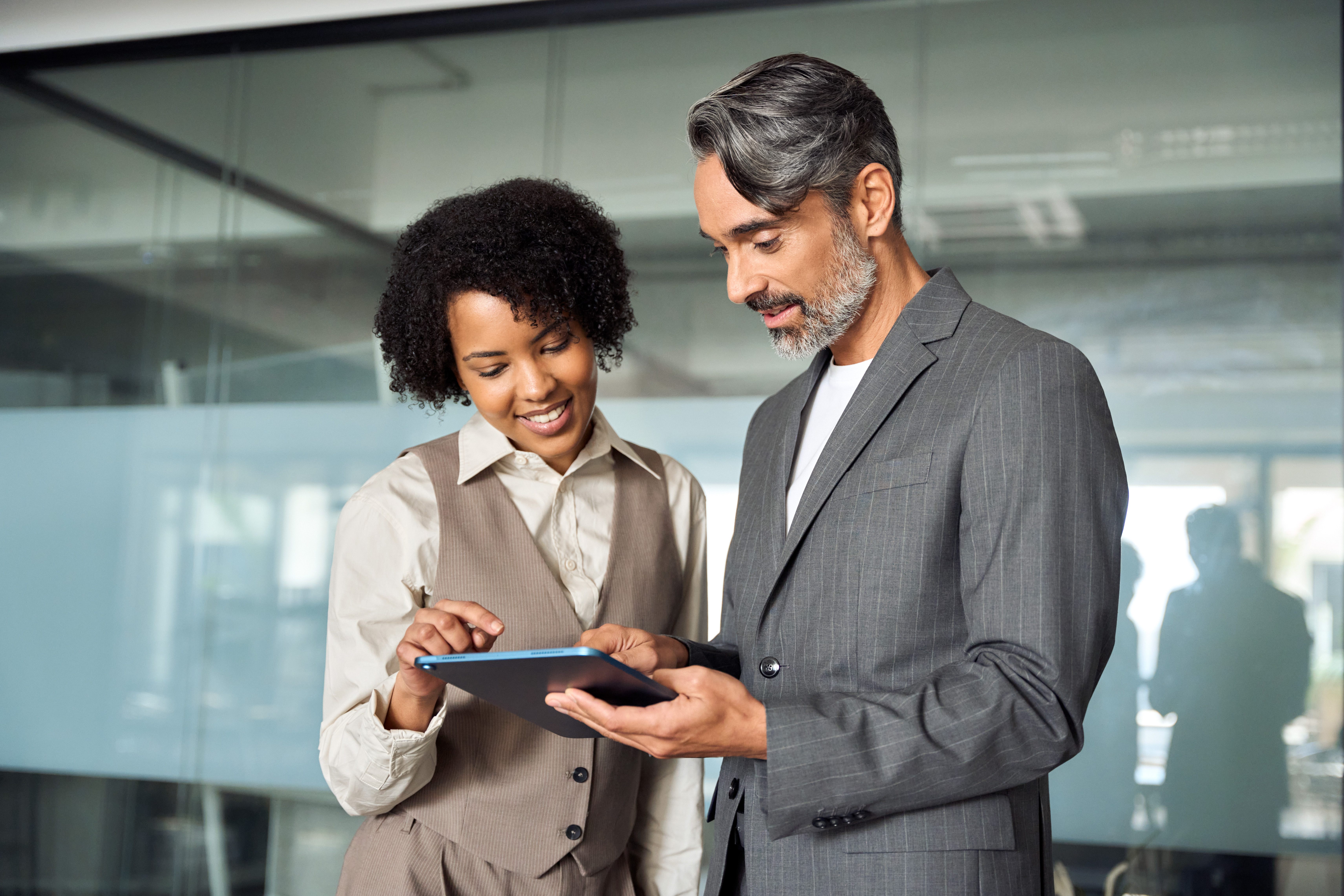 Young female employee and middle-aged male employee standing, looking at tablet