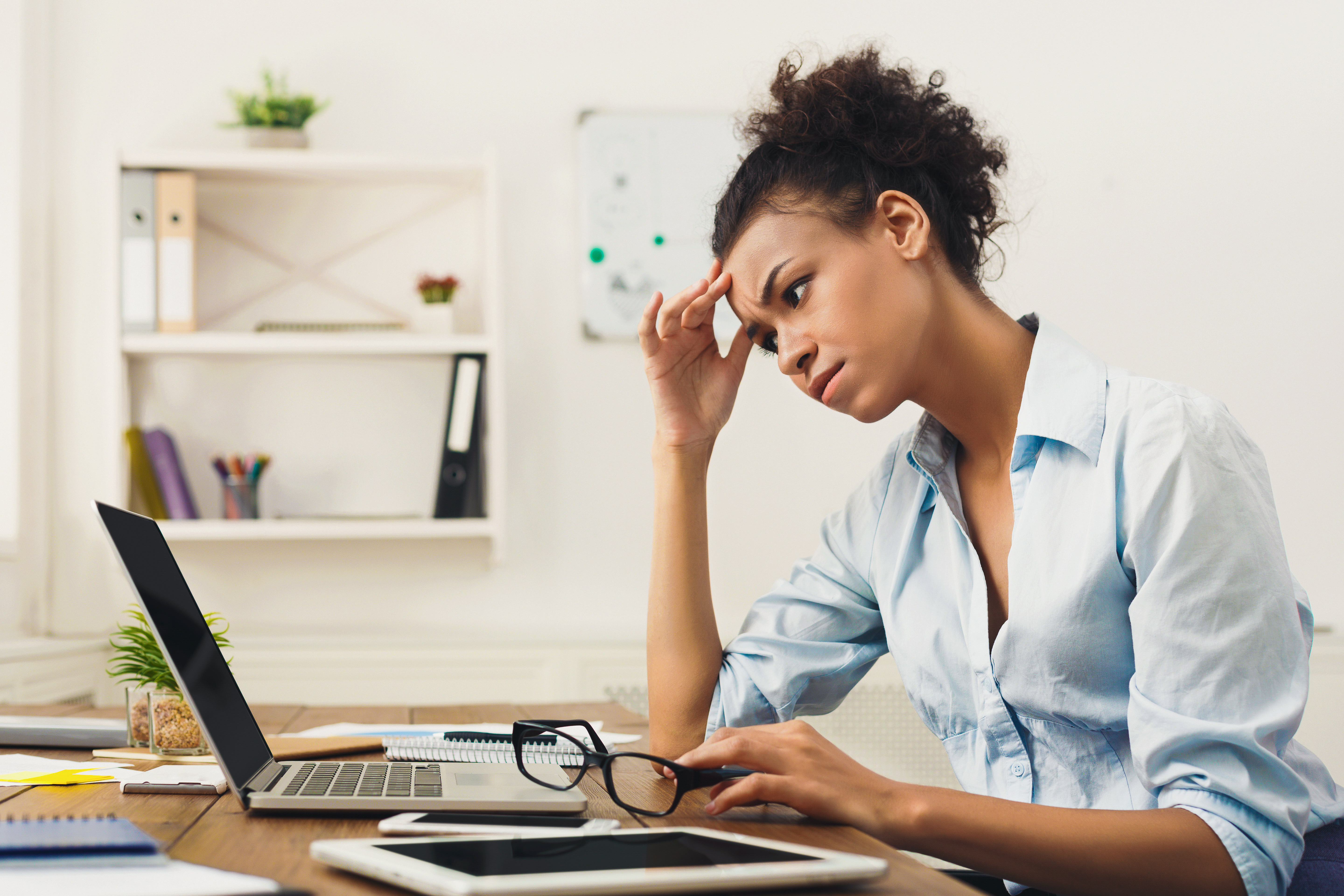 Woman with hand on forehead looking frustrated, sitting at desk with laptop