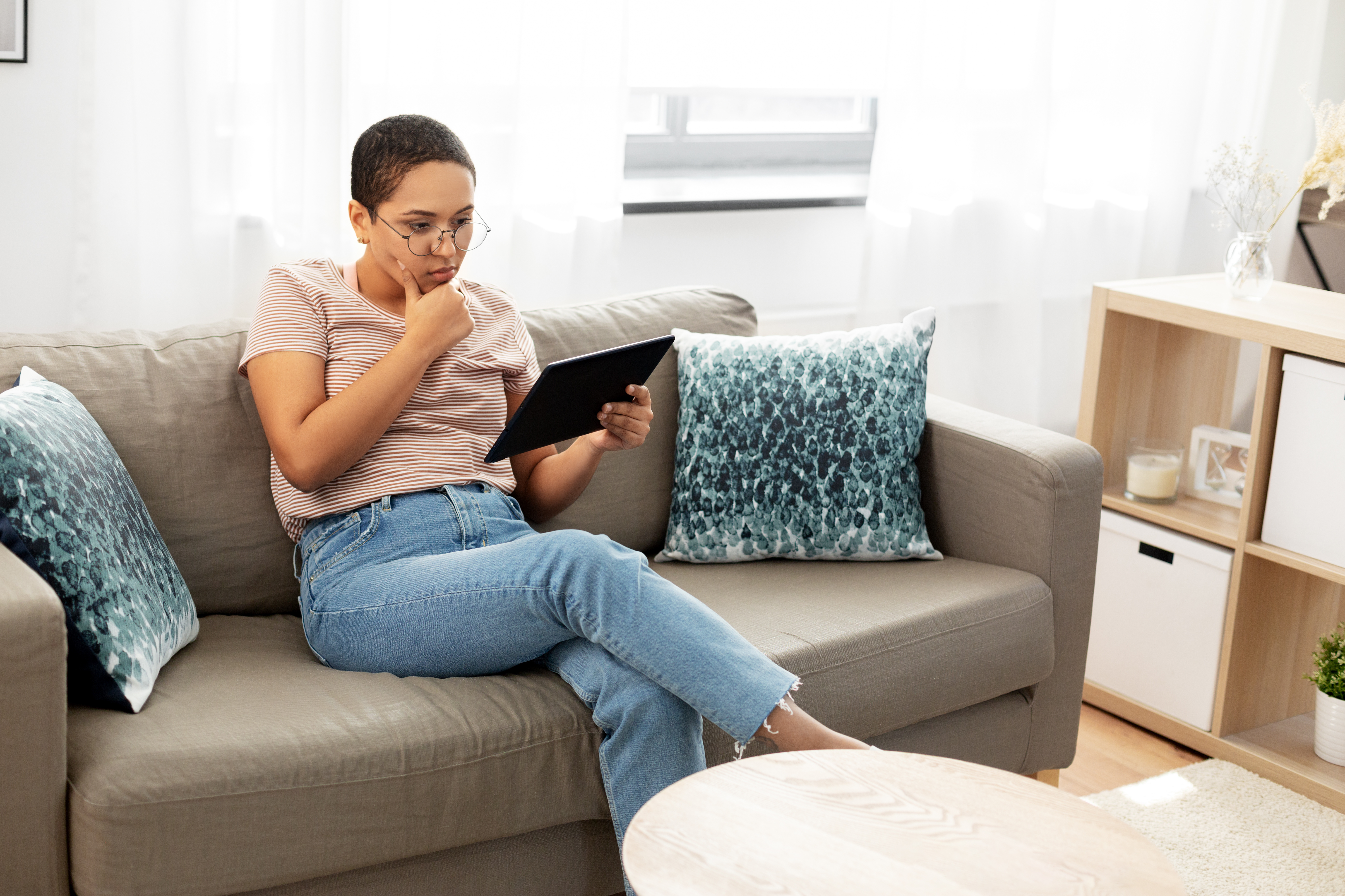Woman sitting on couch looking at tablet, thinking, deciding