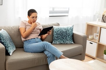 Woman sitting on couch looking at tablet, thinking, deciding