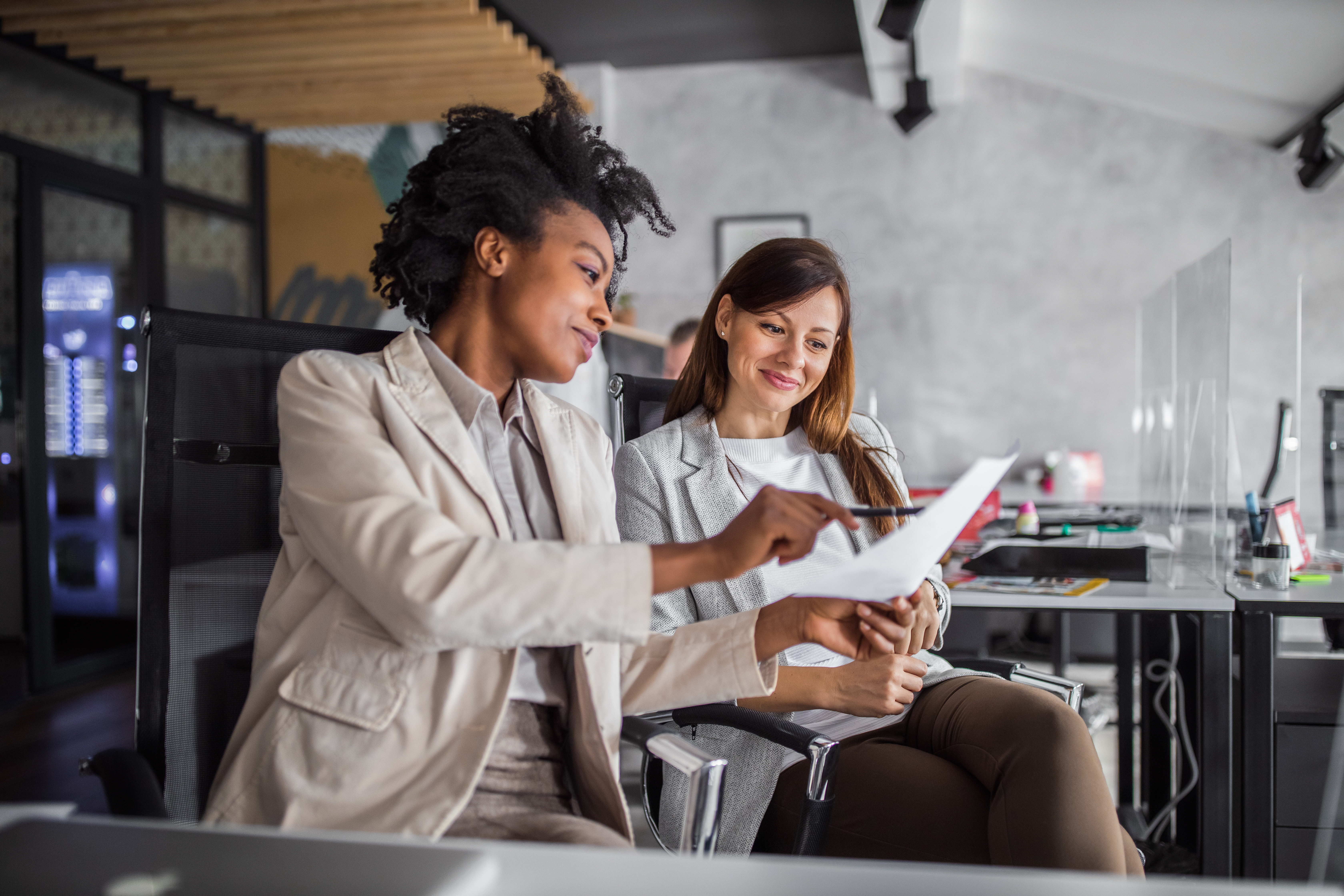 Two women in office looking at paper, smiling