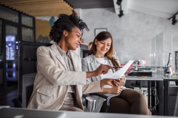 Two women in office looking at paper, smiling