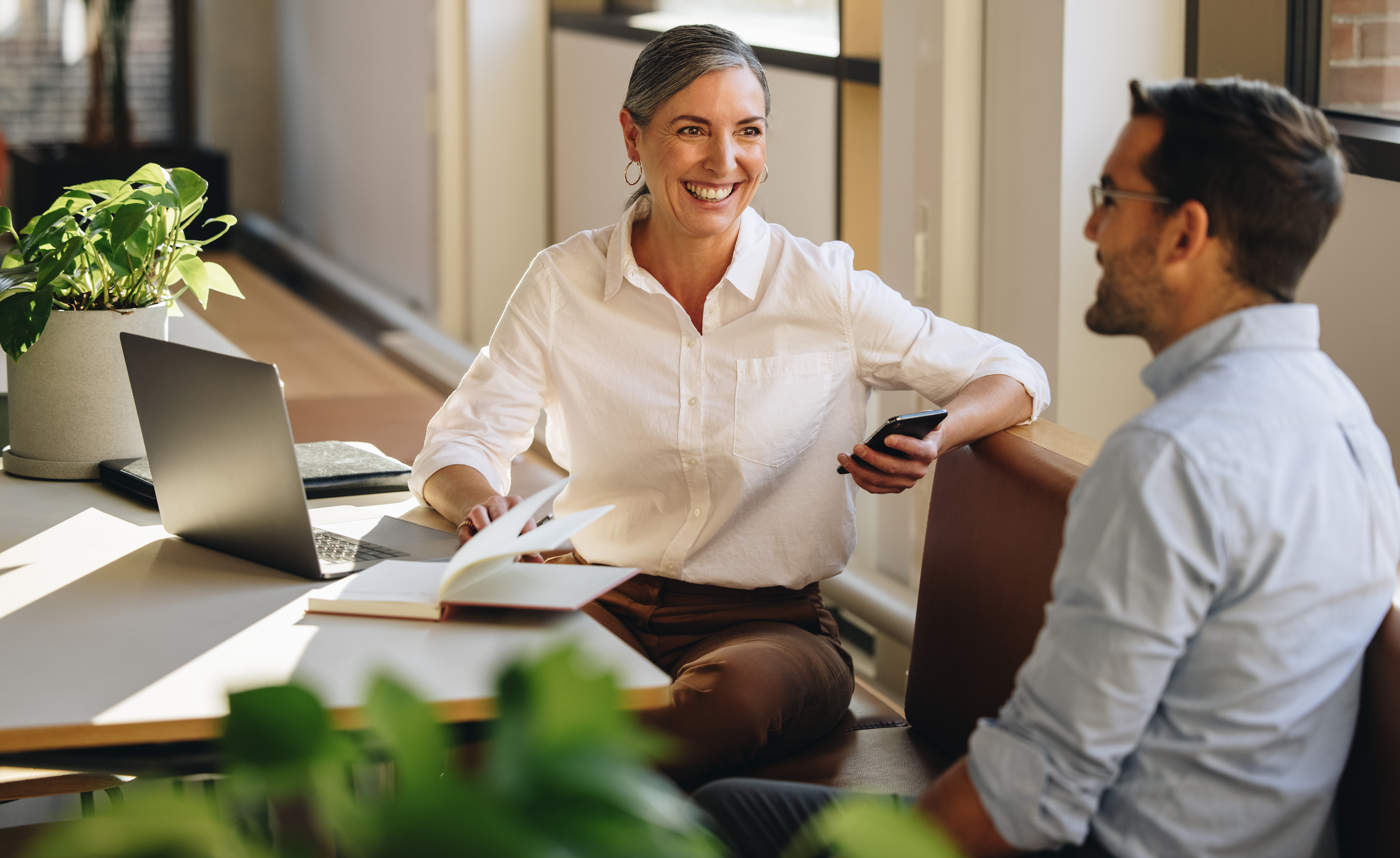 Woman sitting at table, talking to man in office