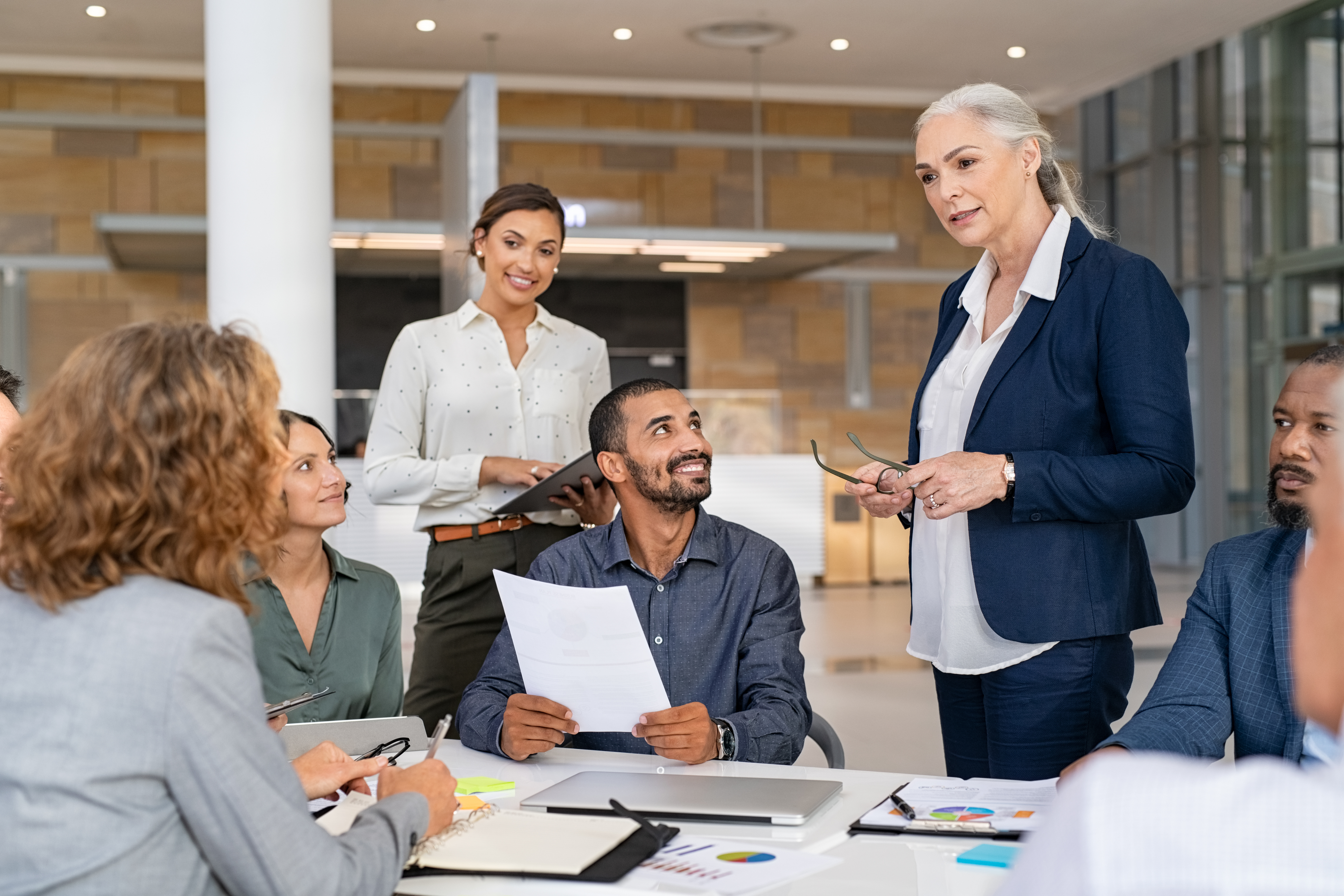 Woman standing, speaking to employees seated at table