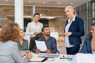 Woman standing, speaking to employees seated at table