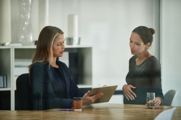 Two female employees talking, looking at clipboard, one pregnant